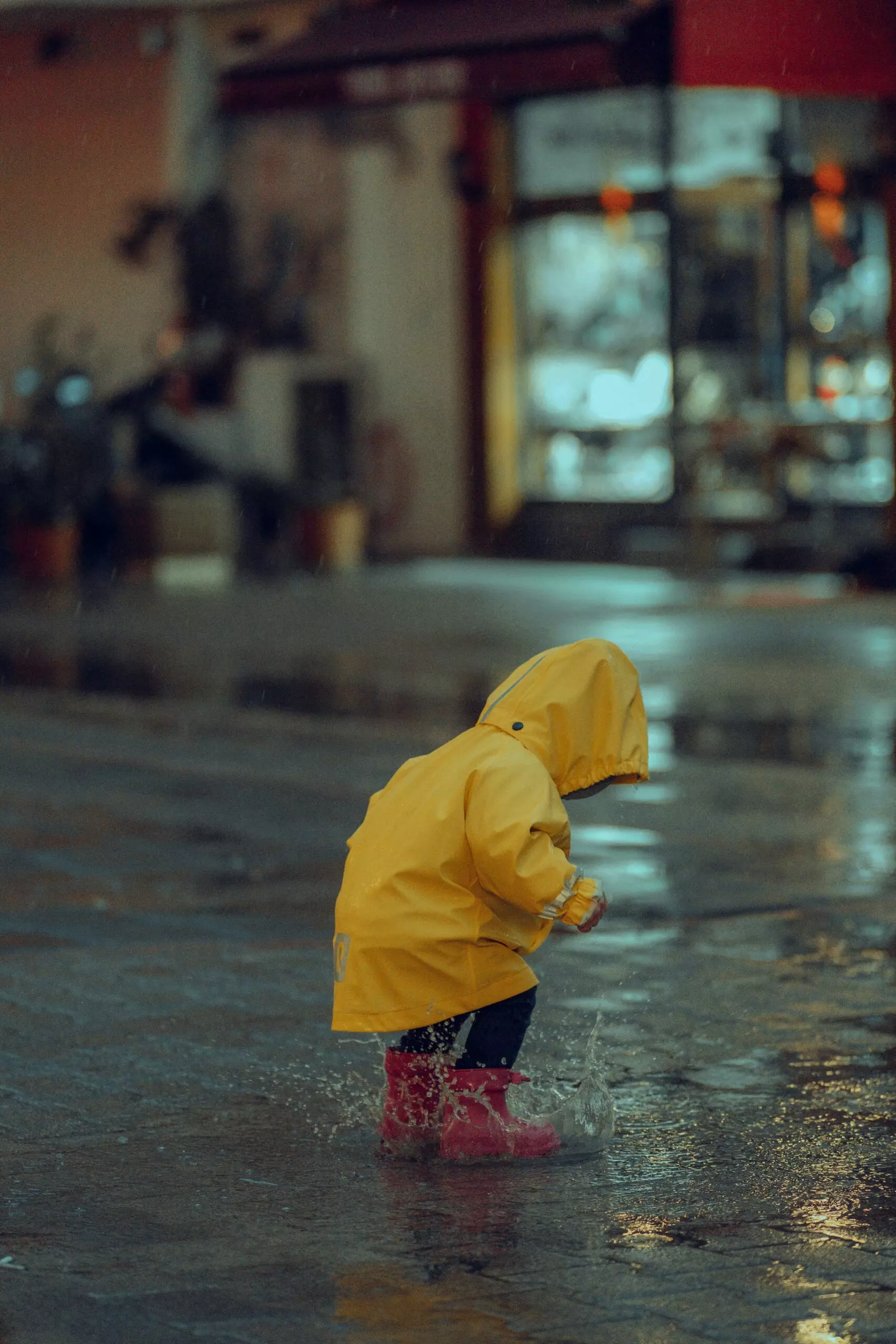 A baby who wear of the yellow raincoat look at the ground.