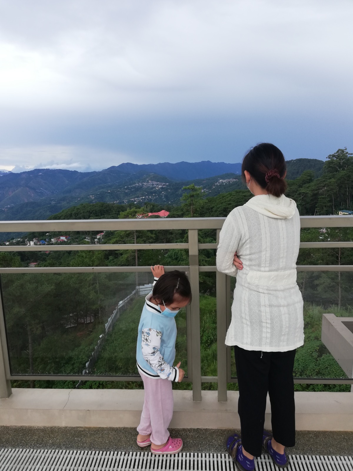 Mother and daughter are looking at the outside scenery from the rooftop