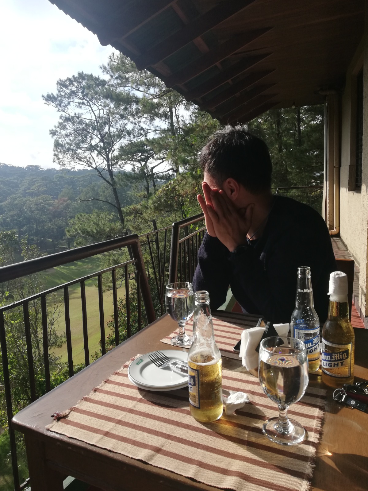 A man is looking at the golf course from the terrace of the restaurant at The Other Office Baguio Country Club.